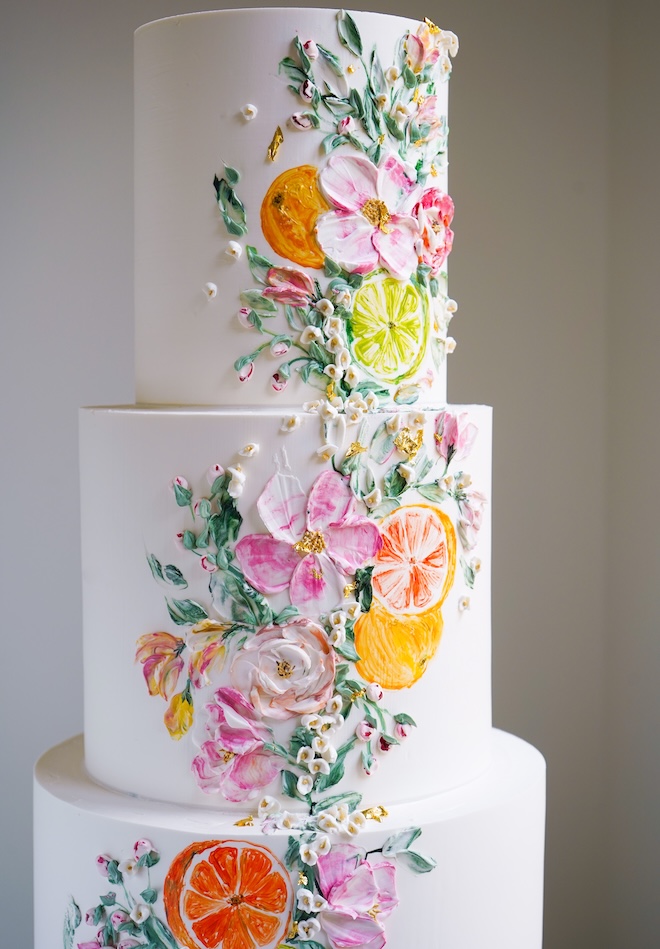 A white wedding cake is hand painted with orange slices.
