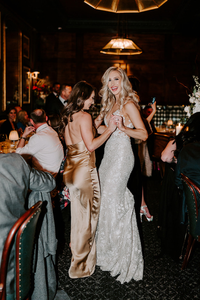 Bride and bridesmaid dancing together in reception venue.