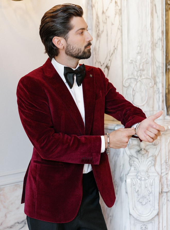 A groom wearing a red velvet suit jacket and a black bow-tie. 