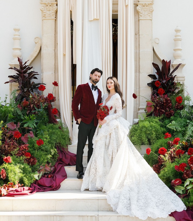 The bride and groom posing at the ceremony space covered in greenery and red florals. 