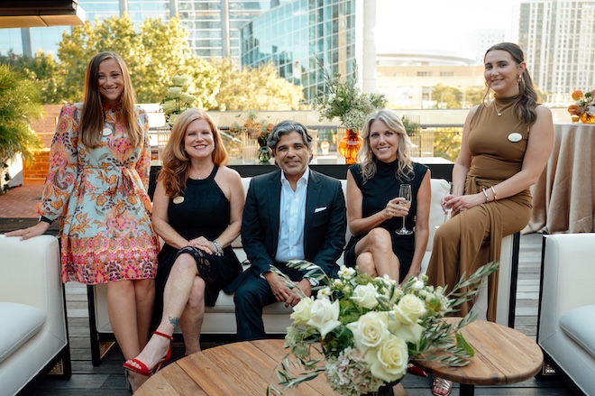 The Weddings in Houston team posing for a picture on a couch with downtown Houston in the background. 