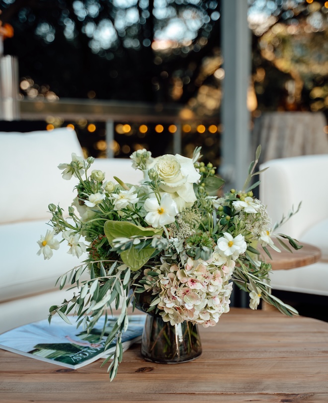 A white and green floral arrangement on a wooden table.