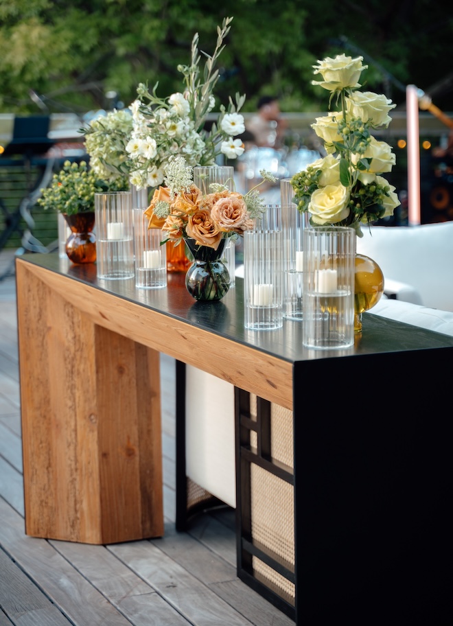 Green, orange and white floral arrangements in bud vases on a table from Caesar Event Rentals. 
