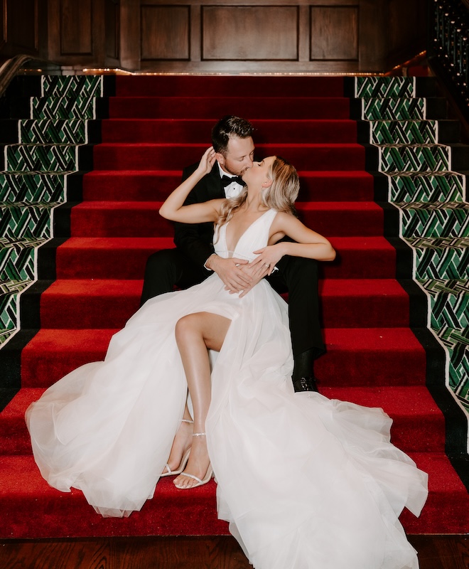 A bride and groom kissing on a red staircase at the Grand Galvez. 