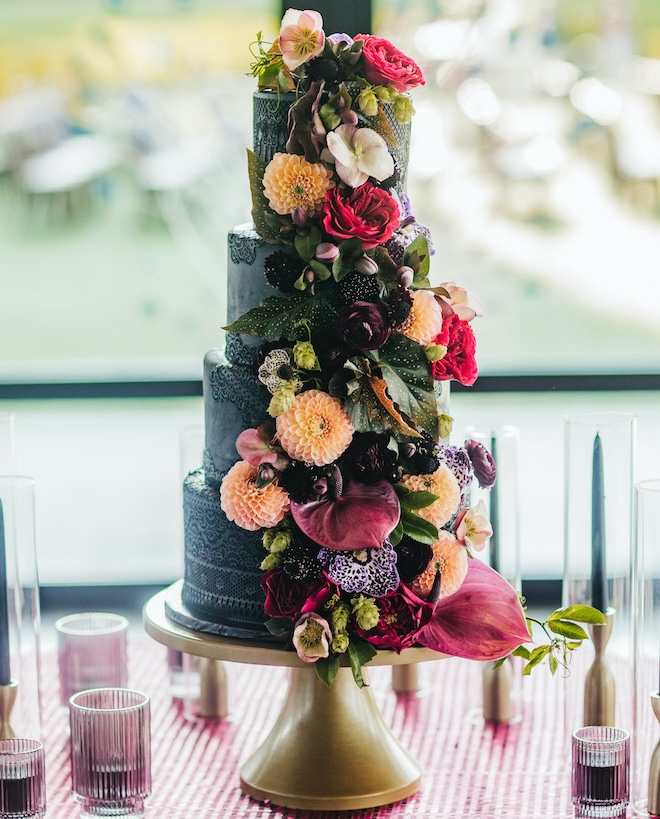 A four-tier black wedding cake with multi-colored florals garnishing the front. 