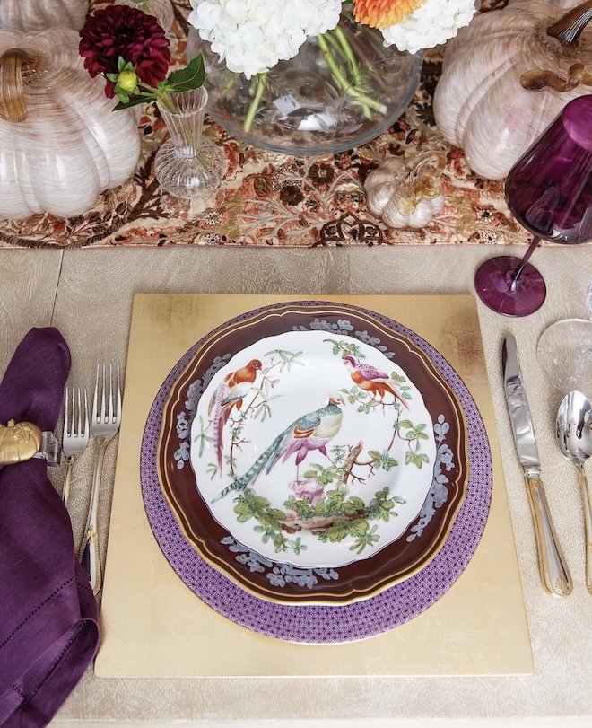 Fine china with birds printed on it are placed on top of purple chargers. 