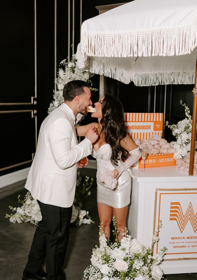 The bride and groom bite into a honey butter chicken biscuit at their reception.