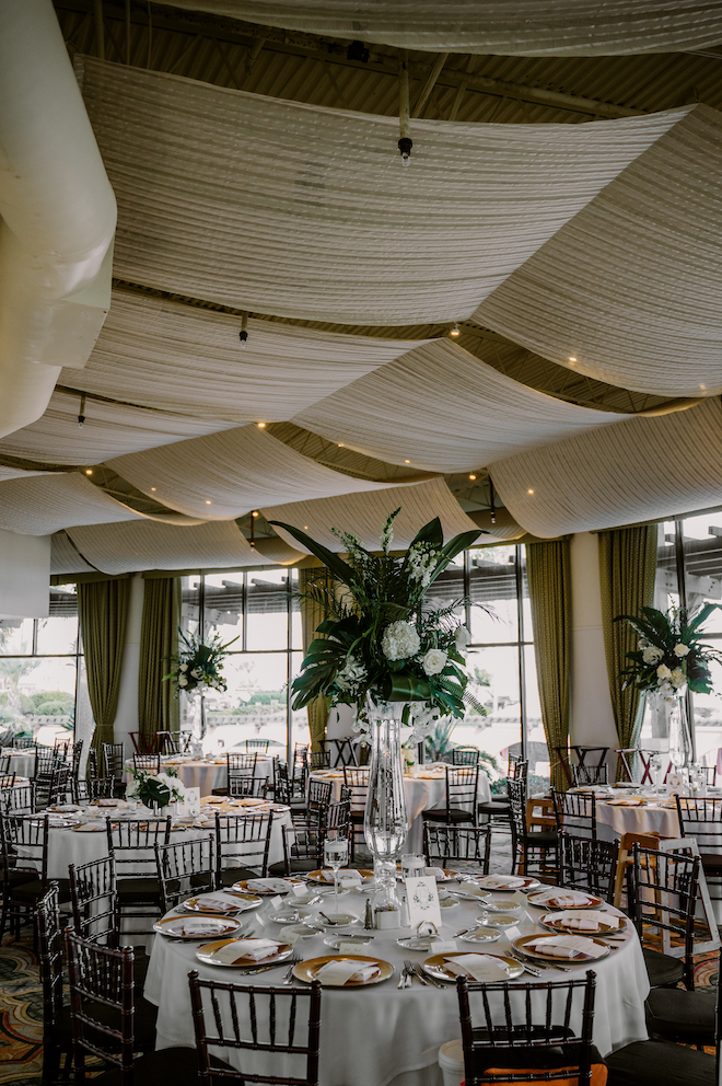 Reception tables with tall green and white bouquets as the centerpieces and white tablecloths.