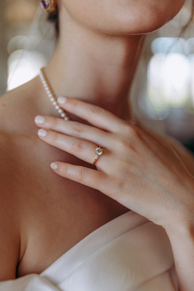 Close up of the bride touching her neck showing her nail, ring and vintage pearl necklace.