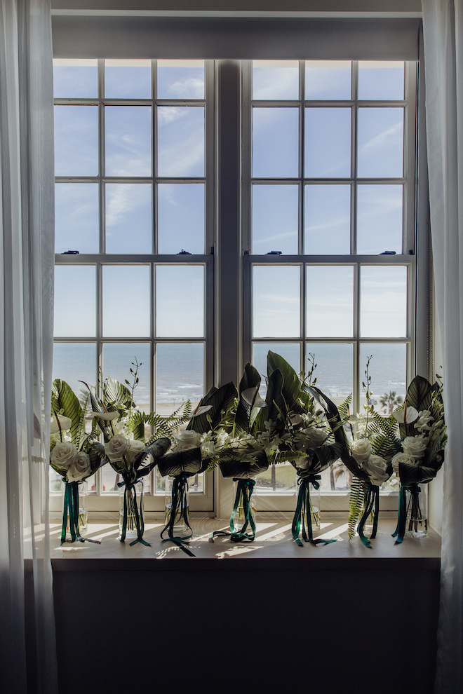 Green and white bouquets standing against window with a view of the ocean.