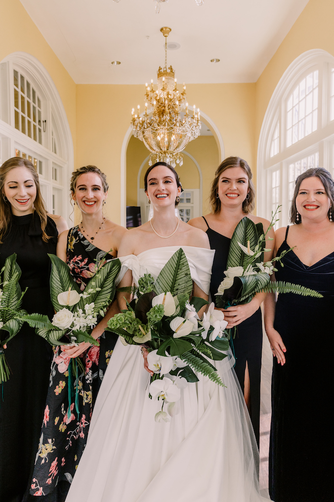 Bride and bridesmaids in the hallway of venue smiling and holding green and white bouquets.