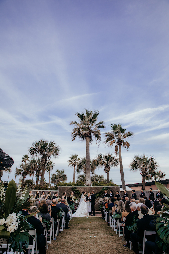 Bride and groom at the altar with tall palm trees behind them.