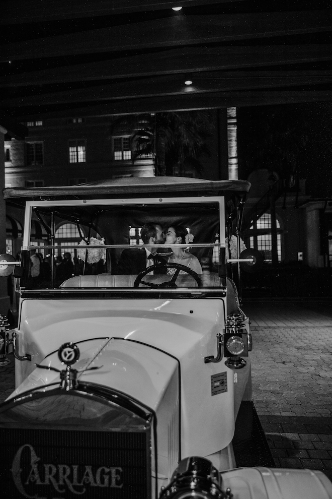 Black and white photo of the couple in the back of vintage getaway car kissing.