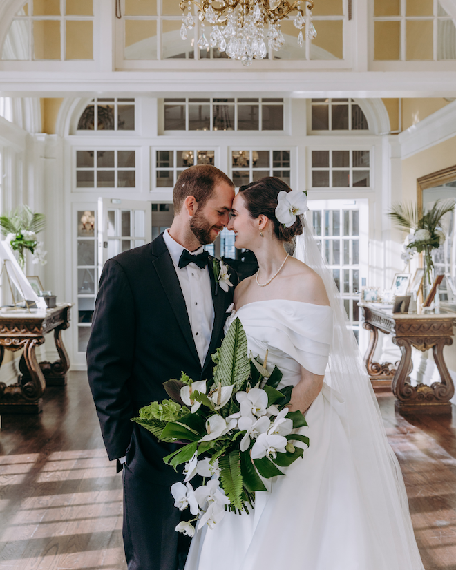 Bride and groom touching foreheads and smiling at each other while bride holds green adn white bouquet.