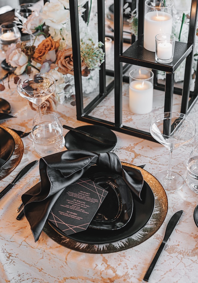Tablescape with gold and black plates, candles and moody-colored florals. 