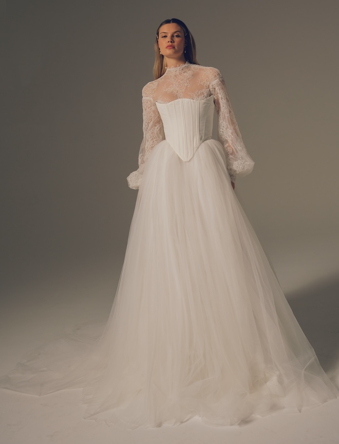 Bride wearing a Hera Couture  high neck Guipure lace blouse with billowing sleeves,  adorned with faux pearl buttons on the sleeves and sheer back.  Paired with a sculpted corset in duchesse satin and a sweeping tulle floral organza skirt. 