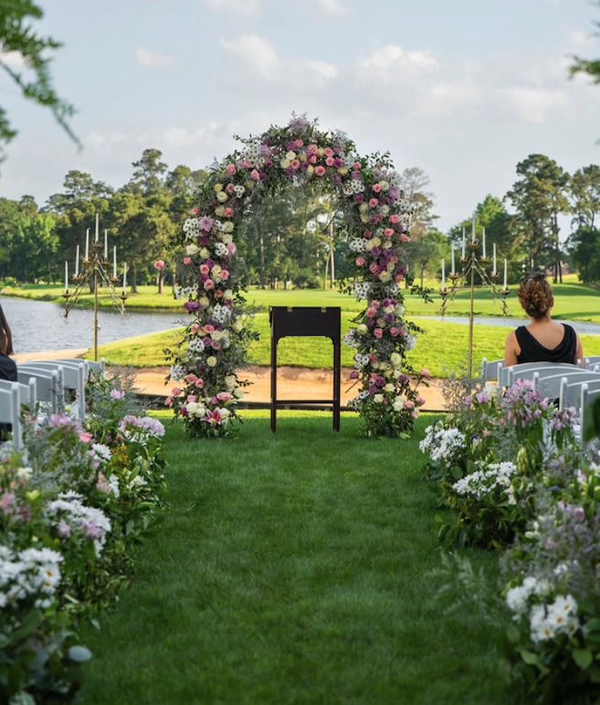 The wedding ceremony has a floral arch with purple, off-white and pink roses.