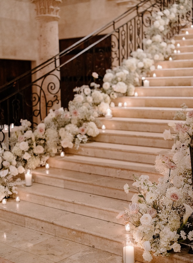 Baby's breath, white florals and blush florals lining a grand staircase with candles. 