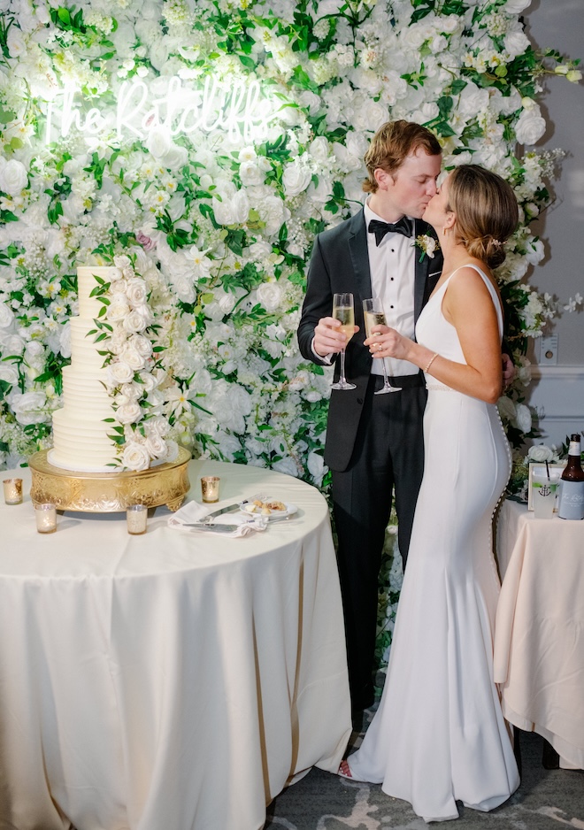 The bride and groom share a kiss next to their wedding cake at their reception.