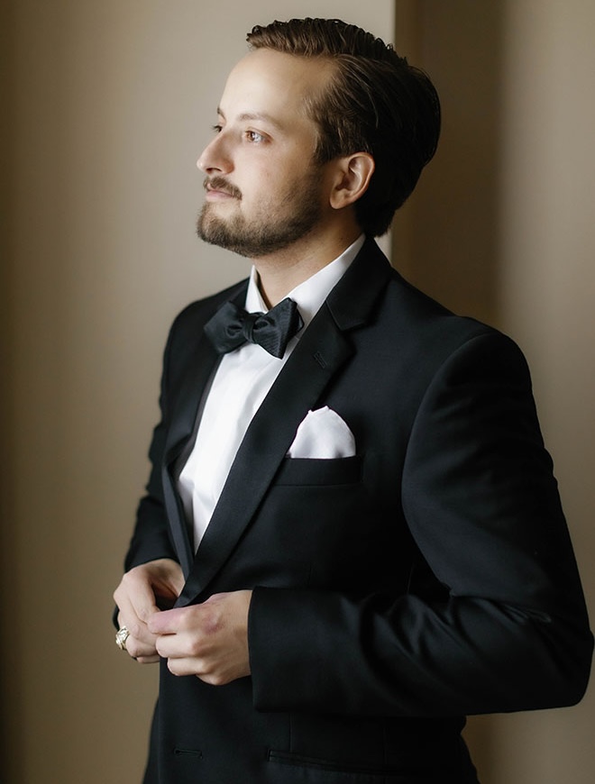 The groom buttons up his tuxedo. 