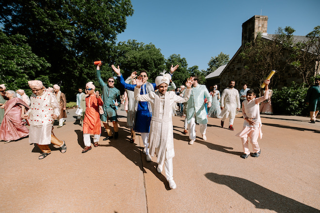 Groom dancing with hands in the air walking into the ceremony with friends and family around him.