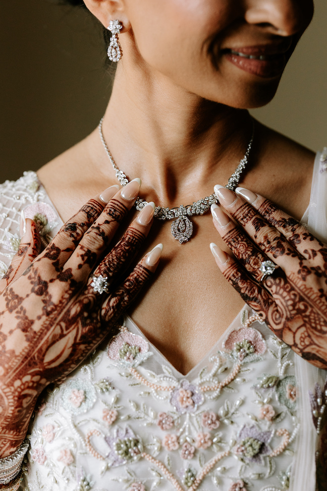 Close up of bride's henna and diamond rings on her chest showing diamond necklace and lehenga neckline.