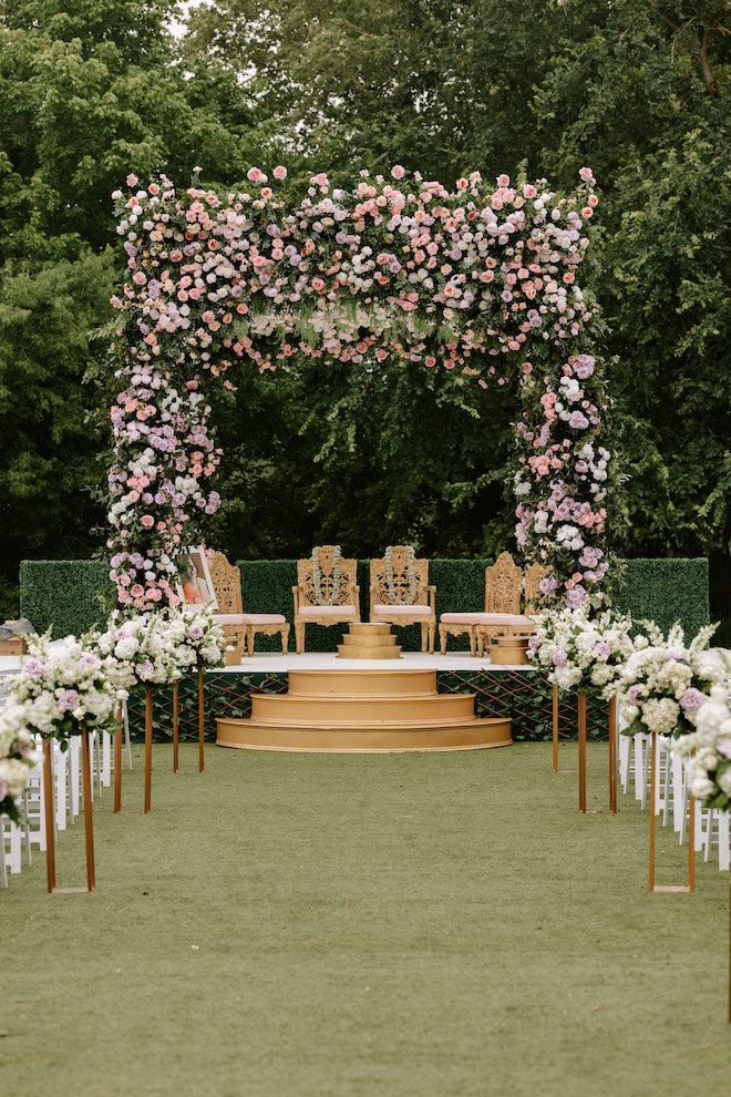 The altar where ceremony is going to be held with chairs at the altar and a big arch with pink and white florals all over it.