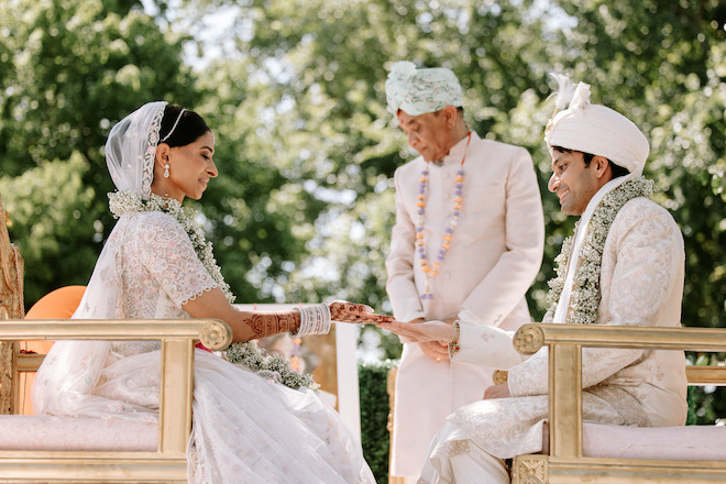 Bride and groom facing each other in chairs outside holding each other's hands.