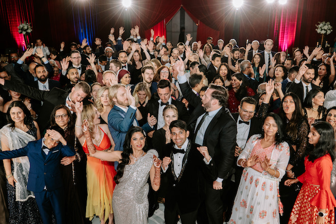 The newlywed couple with guests in vibrant reception venue dancing, smiling, and having fun.