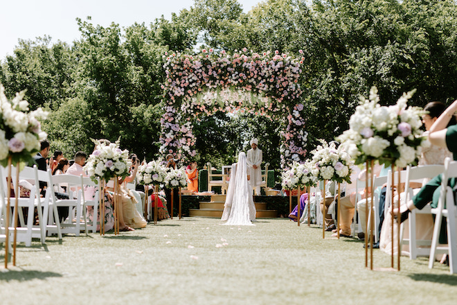 Behind the bride walking up to the altar to the groom with a big lush arch with pink and white florals on it.