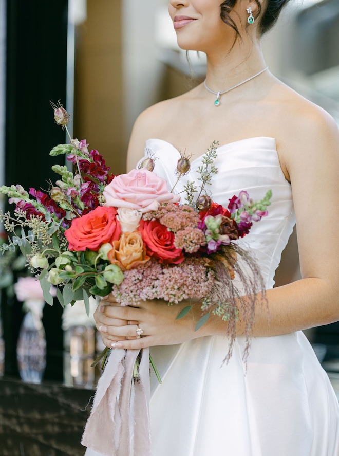 The bride holds her wedding bouquet with purple, pink and coral flowers. 