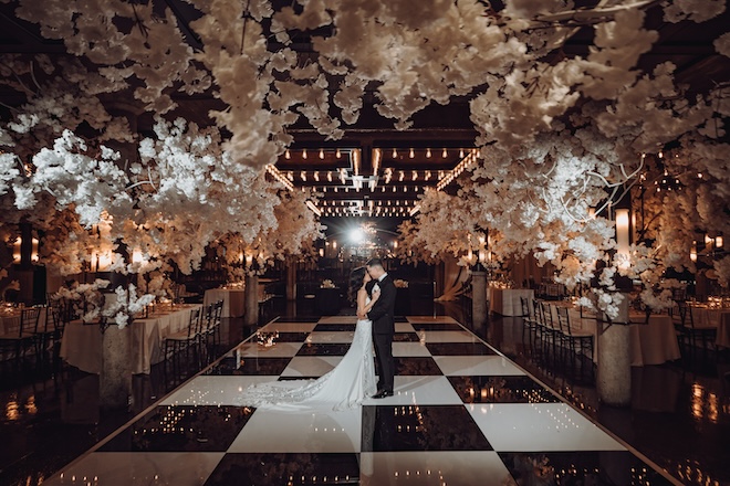 The bride and groom standing on the black-and-white checkered dance floor with white florals surrounding them. 