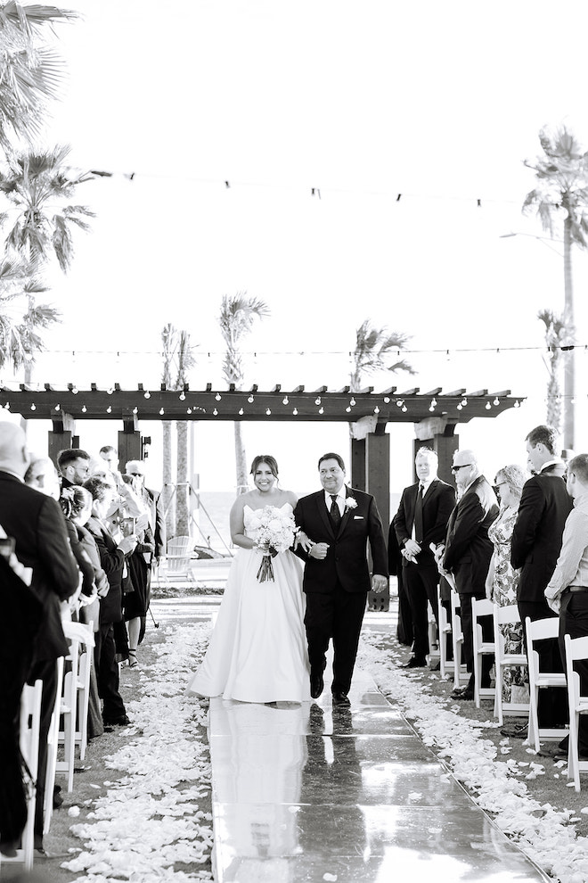 Black and white photo of bride and father of the bride smiling and walking down the aisle.