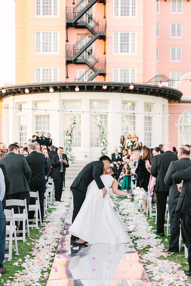 Newlyweds kissing in a dip in the middle of the aisle with flower petals around them.