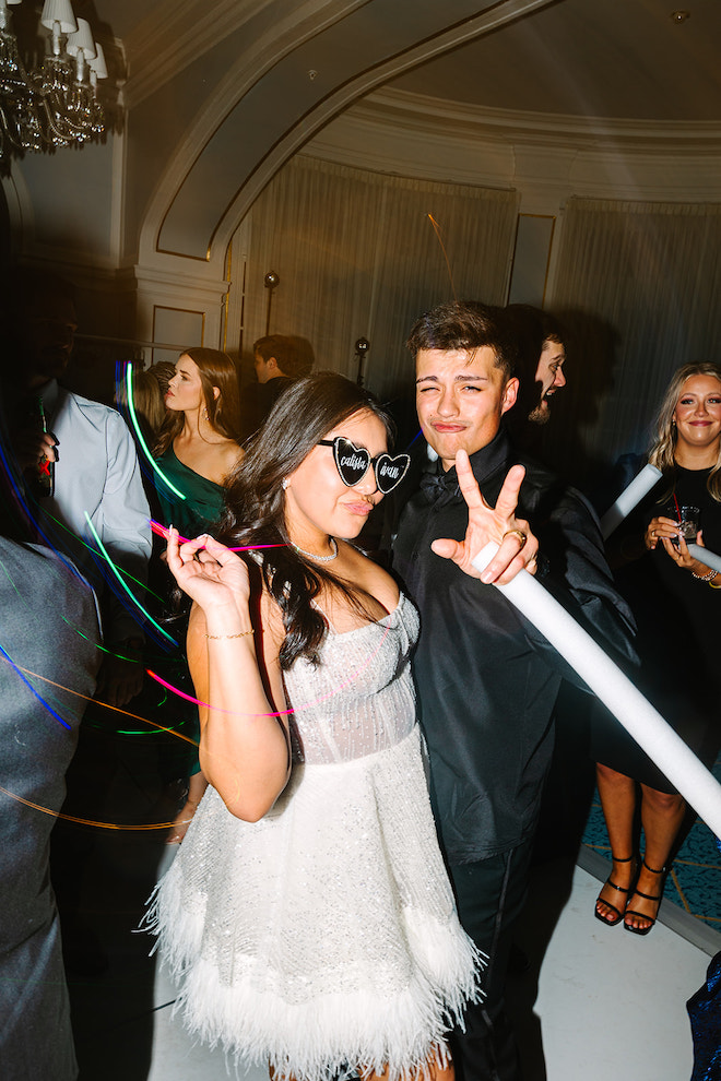 Newlywed couple at the reception holding glowsticks and doing a kissy face at the camera.