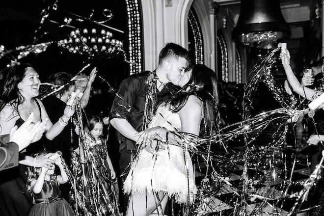 Black and white photo of the bride and groom making their exit in the streamers the guests are holding.