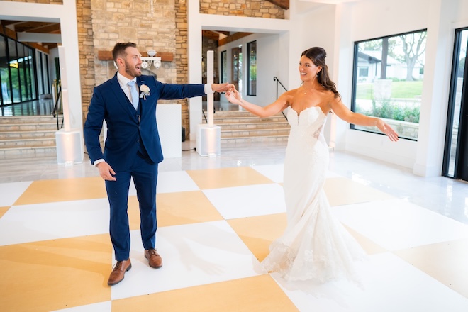The bride and groom share their first dance on a gold and white checkered dance floor.
