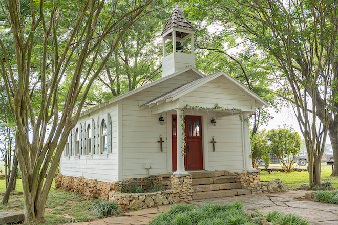 Small white wooden chapel with red doors with stone steps leading up to it.