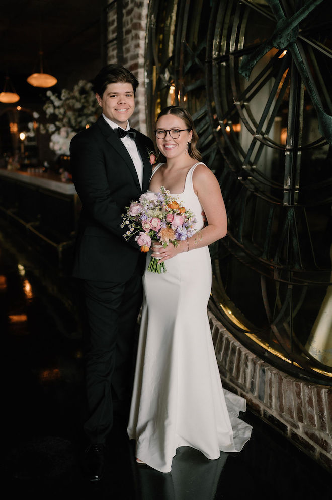 Bride and groom smiling while bride holds pastel floral bouquet.