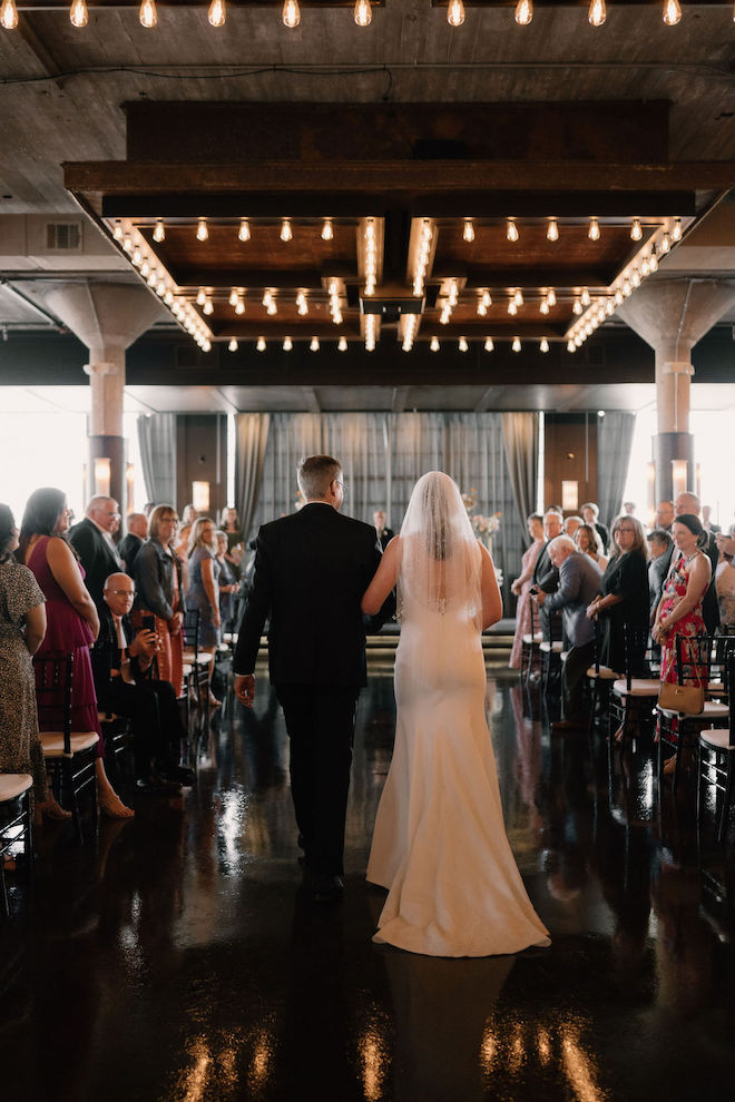 Behind picture of bride and father of the bride walking down the aisle towards the altar.