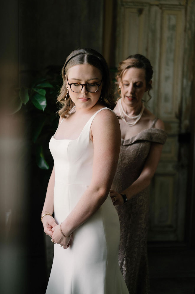 Mother of the bride helping with the bride and her dress in soft lighting.