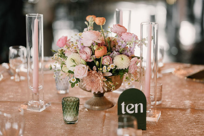 Pastel bouquet centerpiece with sign that reads "table ten" and pink tall candles around it.