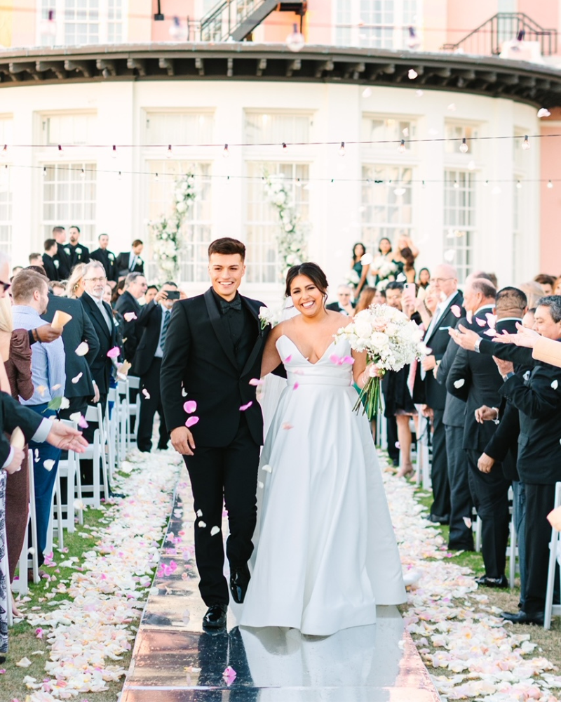 Bride and groom walking down the aisle with pink petals being thrown for them.