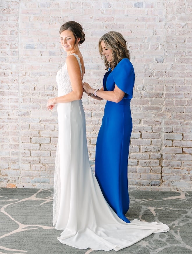 The mother of the bride zips her daughter into her wedding gown.