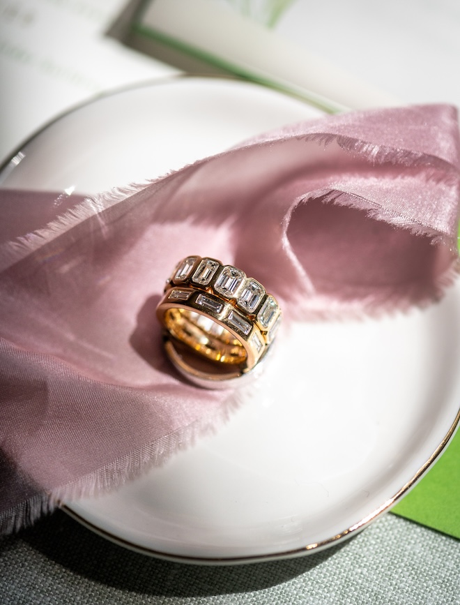 The bride and grooms wedding bands sit on a white plate with pink ribbon.