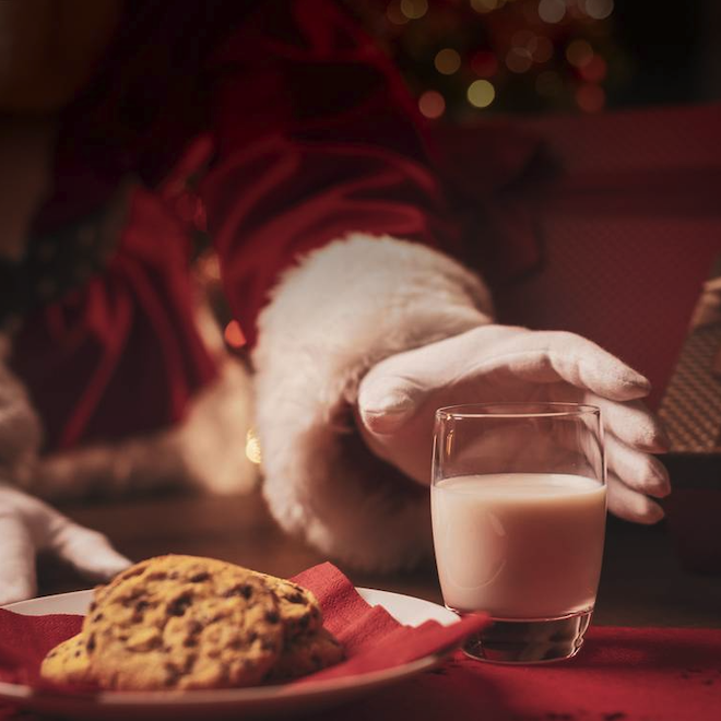 Santa reaching for a glass of milk next to a plate of cookies. 