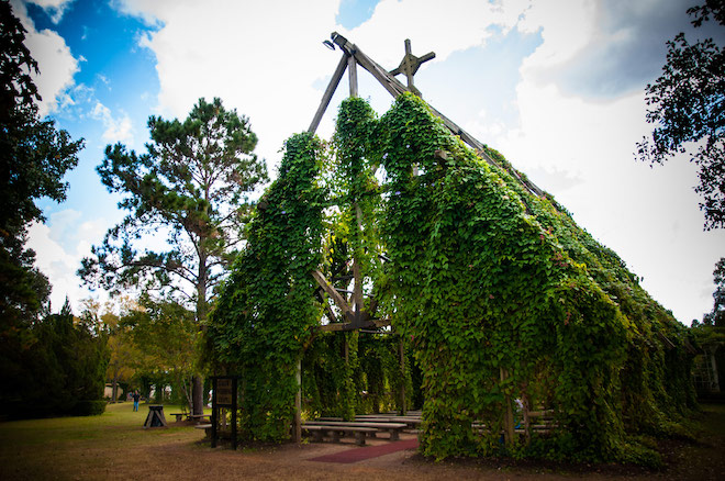 Outside of chapel covered in vines with wooden bench pews inside.