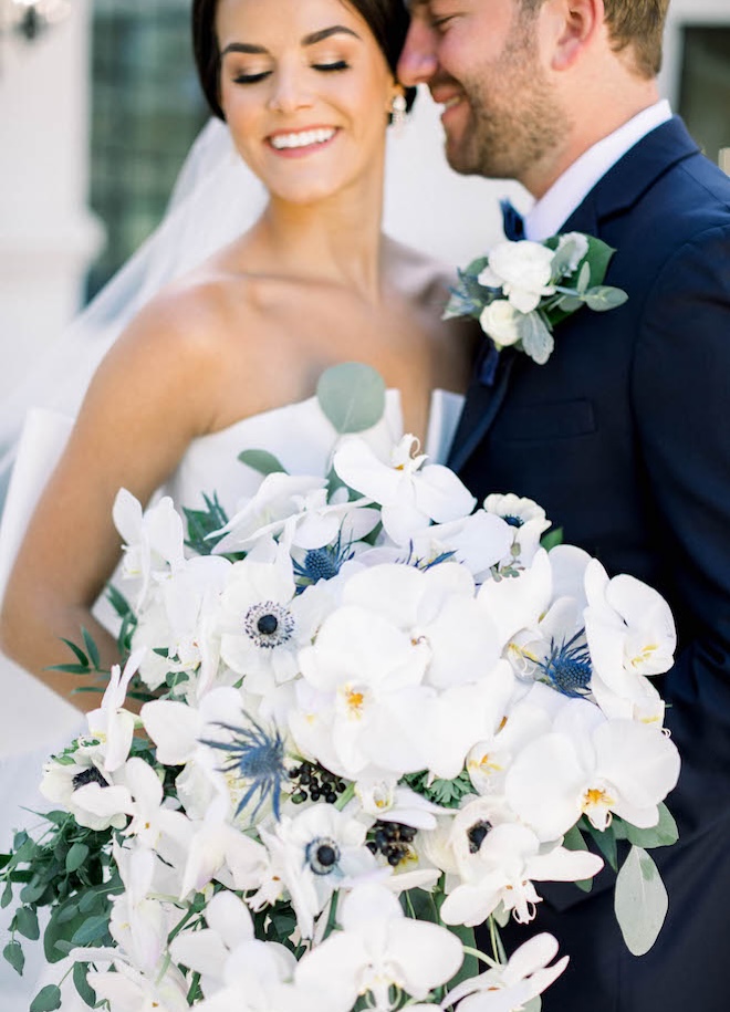 The bride holds her white wedding bouquet with hints of blue florals.