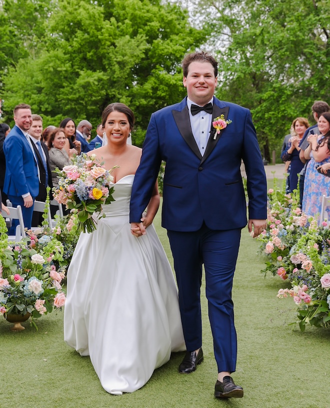 The bride and groom smiling walking back down the english pastel floral lined aisle. 