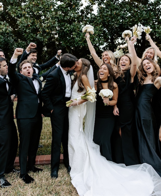 The bride and groom kissing while the wedding party cheers around them. 